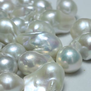 May include: A collection of white baroque pearls with an iridescent sheen. The pearls are various shapes and sizes, and some have a slightly irregular shape.