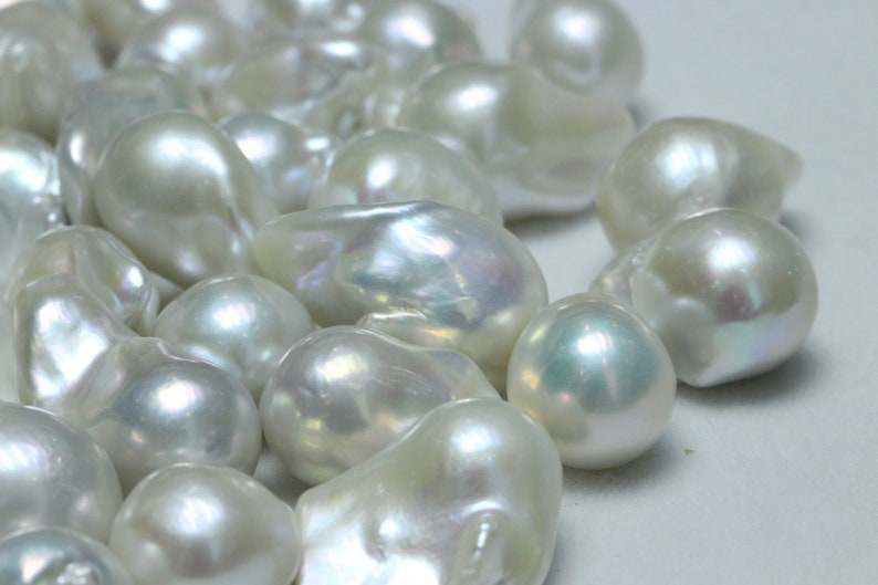 May include: A collection of white baroque pearls with an iridescent sheen. The pearls are various shapes and sizes, and some have a slightly irregular shape.