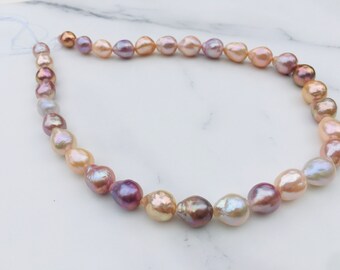 May include: A strand of irregularly shaped, colorful pearls. The pearls display a range of hues, including pink, lavender, and cream, with iridescent surfaces. The pearls are strung together, creating a necklace or bracelet.