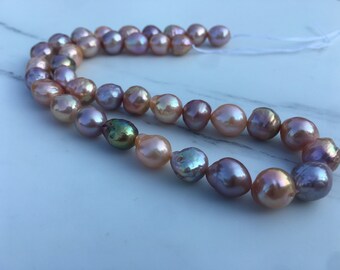 May include: A strand of iridescent pearls in shades of pink, lavender, and green. The pearls are strung on a white cord and are arranged in a loose, flowing pattern.