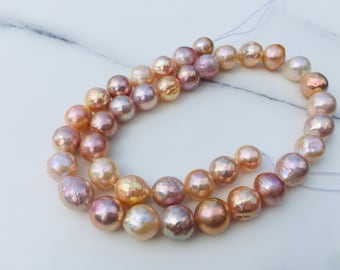 May include: A strand of iridescent pearls in shades of pink, peach, and gold. The pearls are strung on a white thread and are arranged in a circular pattern.