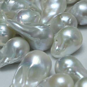 May include: A collection of white, pearlescent, irregular shaped pearls. The pearls are smooth and have a subtle iridescent sheen.