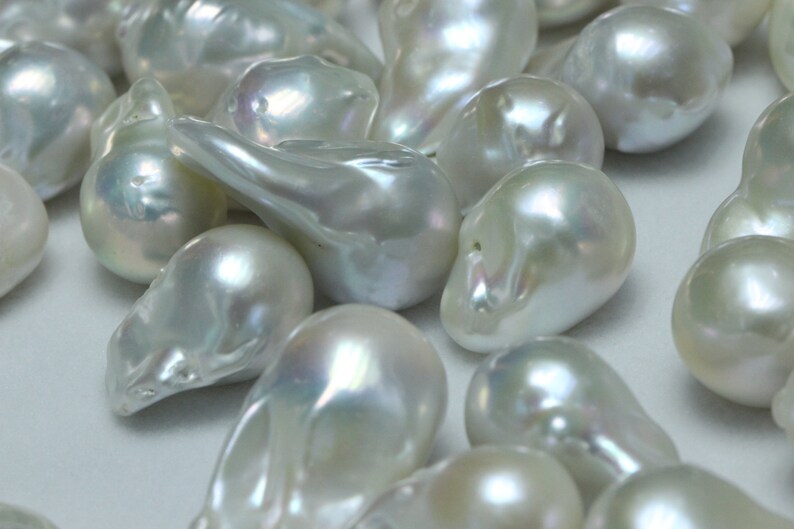 May include: A collection of white, pearlescent, irregular shaped pearls. The pearls are smooth and have a subtle iridescent sheen.