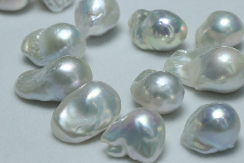 May include: A collection of white baroque pearls with an iridescent sheen. The pearls are various shapes and sizes, and they are arranged in a loose cluster.
