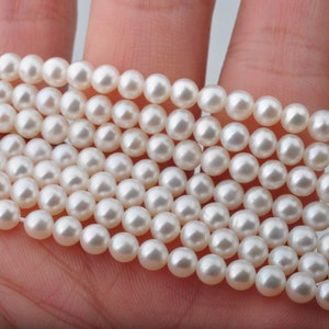 Pode incluir: Um fio de pérolas de água doce brancas, enfiadas em um fio fino. As pérolas são redondas e lisas, com um brilho sutil.