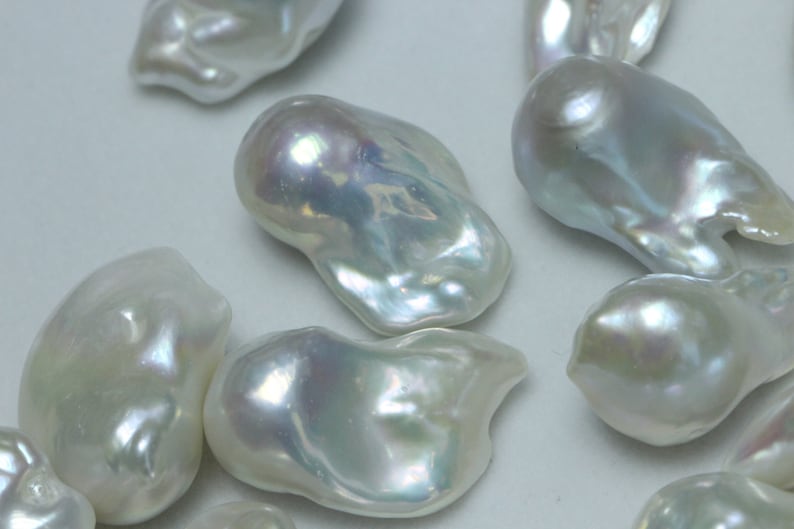 May include: A group of white baroque pearls with an iridescent sheen. The pearls are irregular in shape and have a smooth, glossy surface.
