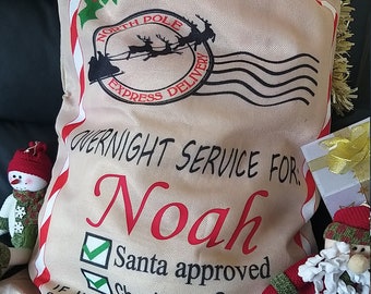 May include: A beige Christmas sack with red and white stripes, a Santa Claus stamp, and the text "OVERNIGHT SERVICE FOR Noah Santa approved ☑ Checked 2x IF UNDELIVERABLE. RETURN TO: SANTA CLAUS. THE NORTH POLE".