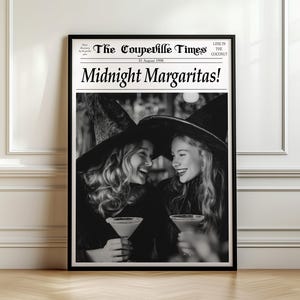 May include: Black and white framed print featuring the headline "Midnight Margaritas!" in a newspaper-style design. The image shows two people wearing witch hats, laughing, and holding cocktails. The print is displayed against a white wall.
