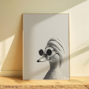 Pode incluir: Uma impressão emoldurada em preto e branco com um pato usando óculos de sol redondos e uma touca de malha. As penas do pato são detalhadas e a imagem tem um fundo neutro. A impressão é exibida em uma sala com uma paleta de cores neutras.