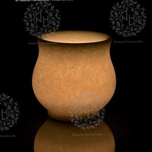 Könnte beinhalten: Handgefertigter, beigefarbener Keramiktopf mit rundem Körper und leicht ausgestelltem Rand. Der Topf hat eine strukturierte Oberfläche und einen dunkelbraunen Rand. Er wird auf einer reflektierenden schwarzen Oberfläche präsentiert. Der Text "Natural Handicrafts" ist sichtbar.