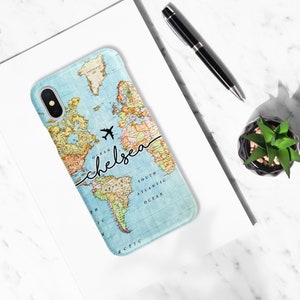 May include: A light blue phone case featuring a world map design with the name "chelsea" in a handwritten font. A black airplane graphic is above the name. The case is on a white surface with a pen and small plant.