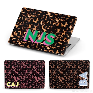 May include: Laptop case with a tortoiseshell pattern and the initials "NJS" in green and pink. Additional cases feature the initials "CAJ" in yellow and "BA" in blue and white. The cases are designed to fit a laptop.