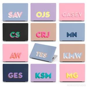 Puede incluir: Una colección de fundas para portátiles en varios colores, cada una con un monograma de tres letras diferente. Las letras son en negrita, estilo 3D, con colores contrastantes. Los fondos son tonos pastel lisos.