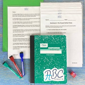 May include: A green composition notebook with a white sticker that says "ABC Crate" on the front. The notebook is wide ruled and has 100 sheets or 200 pages. The notebook is sitting on a wooden table with three highlighters and a pencil.