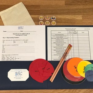 Puede incluir: Una carpeta azul con una hoja de papel blanca en su interior. El papel tiene el t&iacute;tulo "Math Review for Fifth Grade & Level up to 6th Grade". Tambi&eacute;n hay dos l&aacute;pices, una bolsa y varios c&iacute;rculos coloridos con n&uacute;meros en ellos.