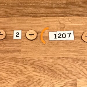 Puede incluir: Un problema de matem&aacute;ticas escrito en tarjetas blancas con s&iacute;mbolos de madera naranja y marr&oacute;n. El problema es 3 x (6814 &divide; 2 - 1207 + 586) = .