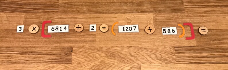 Puede incluir: Un problema de matem&aacute;ticas escrito en tarjetas blancas con s&iacute;mbolos de madera naranja y marr&oacute;n. El problema es 3 x (6814 &divide; 2 - 1207 + 586) = .