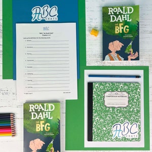 Könnte beinhalten: Ein grünes und schwarzes Kompositionsheft mit einem weißen ABC Crate-Aufkleber. Das Heft liegt auf einer weißen Oberfläche mit einem blauen Bleistift, einem Satz Buntstiften und zwei Exemplaren des Buches "Der BFG" von Roald Dahl.