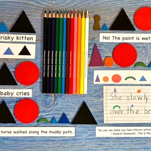 May include: A blue wooden background with various shapes and colors. The shapes include triangles, circles, and semicircles. The colors include blue, red, green, black, and white. There are also pencils and a piece of paper with handwritten text that reads "She slowly walked over the bridge."