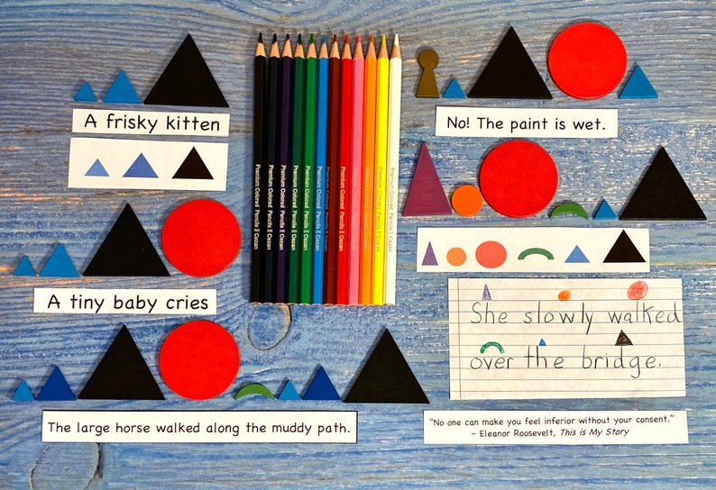 May include: A blue wooden background with various shapes and colors. The shapes include triangles, circles, and semicircles. The colors include blue, red, green, black, and white. There are also pencils and a piece of paper with handwritten text that reads "She slowly walked over the bridge."