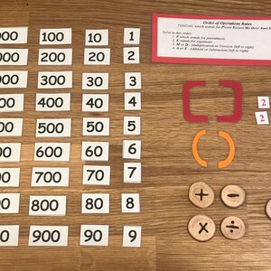 Puede incluir: Un conjunto de manipulativos matem&aacute;ticos para ense&ntilde;ar el orden de las operaciones. El conjunto incluye tarjetas de n&uacute;meros, par&eacute;ntesis, corchetes y s&iacute;mbolos para la suma, la resta, la multiplicaci&oacute;n y la divisi&oacute;n. La mnemot&eacute;cnica "PEMDAS" est&aacute; escrita en una tarjeta, que significa "Please Excuse My Dear Aunt Sally".