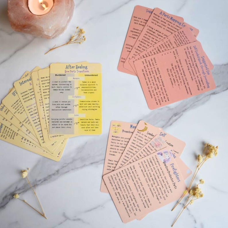 May include: A collection of informational cards with printed text, including titles like After Healing, Parts Mapping Exercise, and Firefighter Protector Parts. The cards are arranged in three distinct stacks on a white surface, featuring yellow and peach-colored paper with black text and small illustrations.