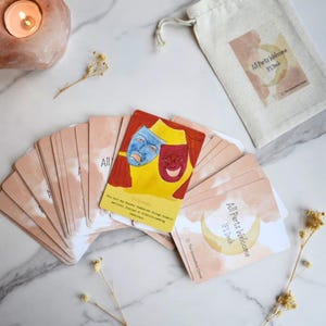 May include: A deck of All Parts Welcome IFS cards with a beige drawstring bag. One card features a yellow background with red curtains and blue and red theatrical masks. Other cards show a crescent moon and the text All Parts Welcome IFS Deck.