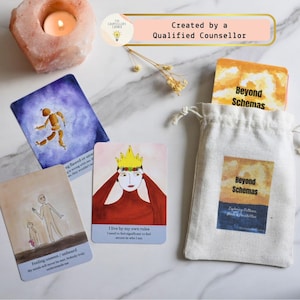 May include: Oracle cards with watercolour illustrations and text, including "Beyond Schemas" and "I live by my own rules." The cards are in a drawstring bag, with a lit candle and a decorative stone in the background.