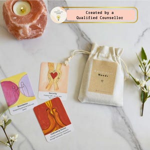 May include: A collection of relational needs cards featuring illustrations and text, such as "Boundaries," "Security," and "Cultivating Desire." A small drawstring bag marked "Relational Needs" is visible, alongside a lit candle and a decorative stone.