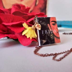 Pu&ograve; includere: Una collana d'oro con un piccolo ciondolo a forma di libro che presenta un ritratto di Frida Kahlo e la parola "FRIDA" sulla copertina. Il ciondolo del libro &egrave; attaccato a una catena delicata con un piccolo ciondolo a forma di fiore.