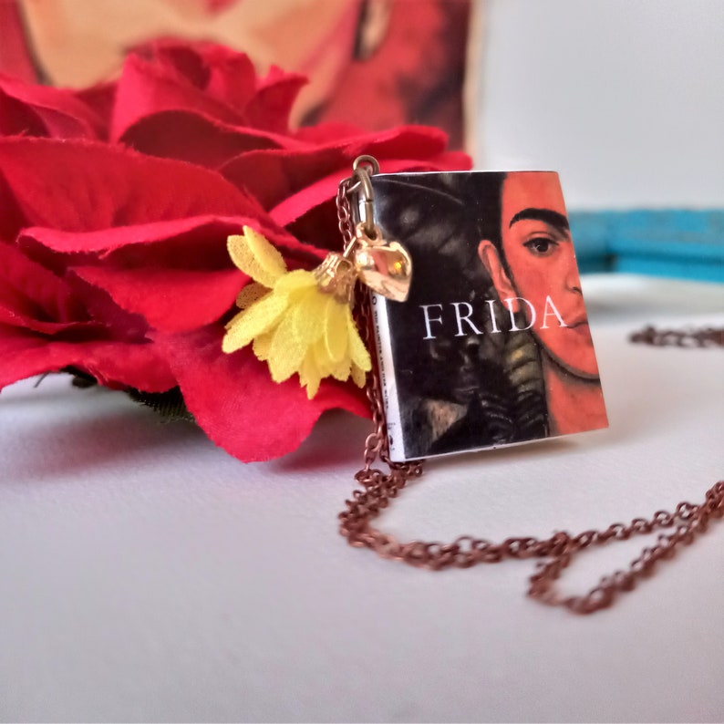 Pu&ograve; includere: Una collana d'oro con un piccolo ciondolo a forma di libro che presenta un ritratto di Frida Kahlo e la parola "FRIDA" sulla copertina. Il ciondolo del libro &egrave; attaccato a una catena delicata con un piccolo ciondolo a forma di fiore.