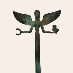 Puede incluir: Una estatua de bronce verde de una figura femenina alada con un búho en una mano y una luna creciente en la otra. La estatua está sobre una base de mármol negro.