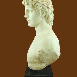 K&ouml;nnte beinhalten: Cremefarbene B&uuml;ste einer Person mit lockigem Haar und einem Lorbeerkranz. Die Skulptur ist auf einem schwarzen, rechteckigen Sockel montiert. Die B&uuml;ste ist ein Seitenprofil, das die Gesichtsz&uuml;ge der Person zeigt.
