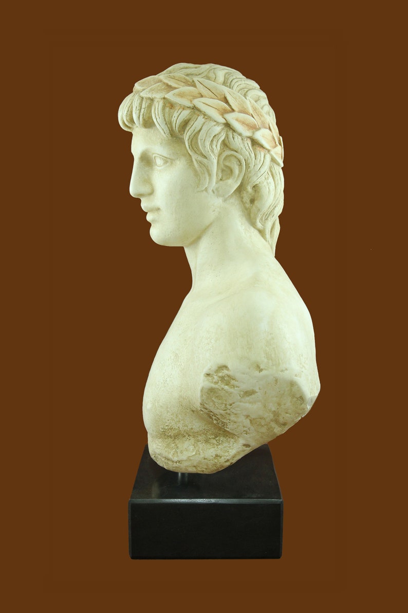 K&ouml;nnte beinhalten: Cremefarbene B&uuml;ste einer Person mit lockigem Haar und einem Lorbeerkranz. Die Skulptur ist auf einem schwarzen, rechteckigen Sockel montiert. Die B&uuml;ste ist ein Seitenprofil, das die Gesichtsz&uuml;ge der Person zeigt.