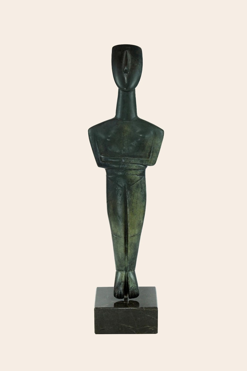 May include: A green bronze sculpture of a standing figure with a simplified, geometric design. The figure has a long neck, a small head, and arms crossed at the chest. The sculpture is mounted on a black marble base.