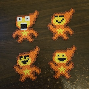 May include: Four orange pixel art figures with different facial expressions. Each figure has a flame-shaped head and a small body with arms and legs. The figures are made of small, colorful beads.