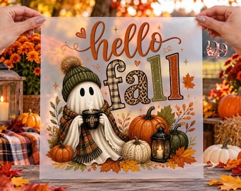 May include: A transparent transfer sheet featuring a ghost wearing a green knit hat and plaid scarf, holding a coffee mug. The text reads hello fall in orange, black plaid, and leopard print. Surrounded by pumpkins, leaves, and a lantern.