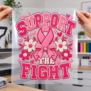 May include: A clear transfer sheet featuring a pink and white design with the text SUPPORT THE FIGHT in a bold, textured font. The graphic includes a central pink awareness ribbon, surrounded by pink and white flowers, hearts, and stars.