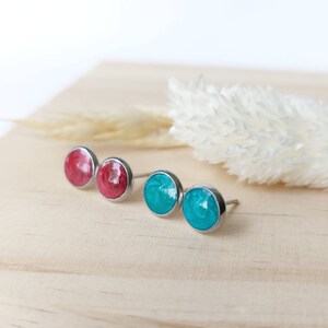 Op de afbeelding: Een set van vier oorbel studs met een zilveren achterkant. Twee oorbel studs zijn een levendige rode kleur en de andere twee zijn een heldere turquoise.