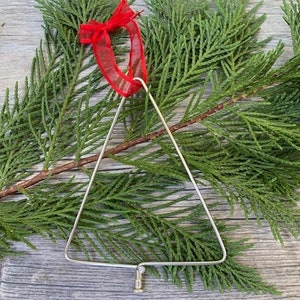 May include: A silver wire Christmas tree ornament with a red ribbon attached to the top.