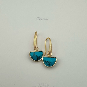 Puede incluir: Un par de pendientes de oro con piedras turquesa. Las piedras tienen forma semicircular y presentan un patrón de mármol. Los pendientes cuelgan de un gancho de oro.