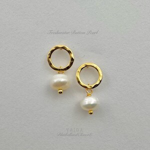 May include: A pair of gold hammered hoop earrings with a freshwater button pearl dangling from each hoop.