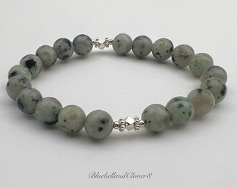 May include: A green and white speckled stone bracelet with silver accents. The bracelet is made of round beads and has a clasp.