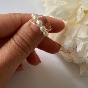 May include: A delicate silver ring with a row of white pearls. The ring is worn on a finger.