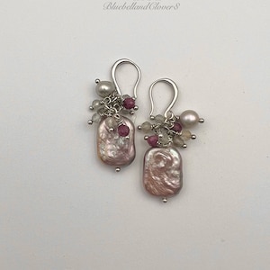 May include: A pair of silver earrings featuring pink and white pearl-like stones and pink and white beads. The earrings are labelled "VAIDA Bluebelland Clovers".