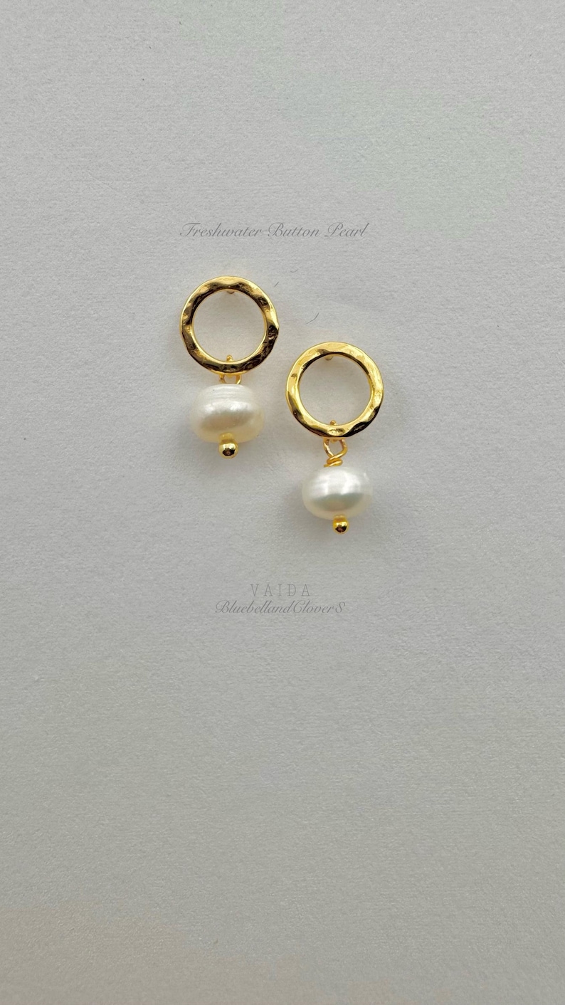 May include: A pair of gold hammered hoop earrings with a freshwater button pearl dangling from each hoop.