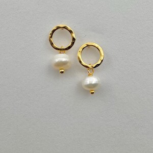 May include: A pair of gold hoop earrings with a small white pearl dangling from each hoop.