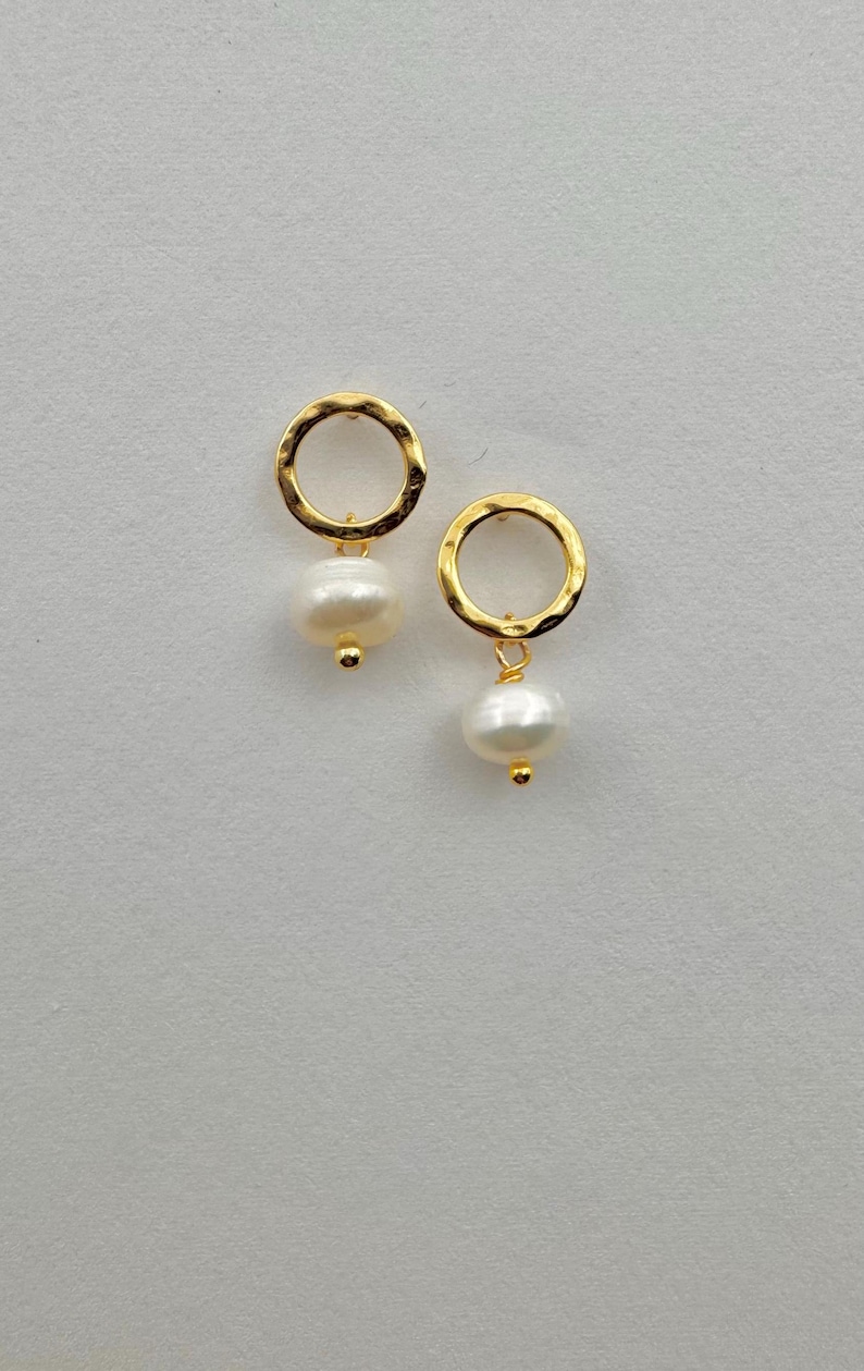 May include: A pair of gold hoop earrings with a small white pearl dangling from each hoop.