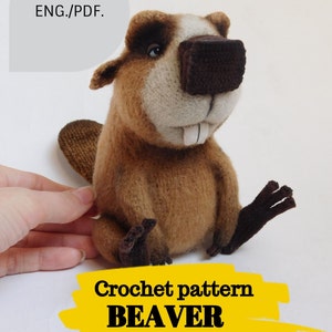 Pode incluir: Padrão de crochê para um castor marrom com nariz branco e olhos castanhos. O castor está sentado com as patas à sua frente. O texto "Crochet pattern BEAVER" está em um fundo amarelo.