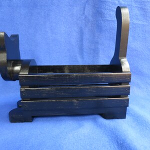 May include: Black wooden dog-shaped storage basket. The basket has a rectangular body with horizontal slats and a curved handle. The dog's head and tail are also part of the design. The basket is painted black with a distressed finish.